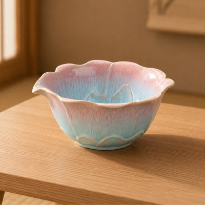Matcha tea bowl with lotus-shaped scalloped rim and pink-to-turquoise drip glaze on a light wood table in a warm Japanese interior
