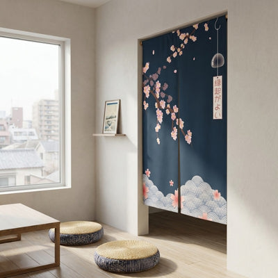 Noren curtain blue with navy background pink cherry blossom branches glass furin wind chime and seigaiha cloud border displayed in minimalist Japanese room with low table floor cushions and city rooftop view
