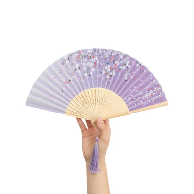 Person wearing cream kimono holding paper japanese folding fan with lavender background and white sakura in traditional interior setting