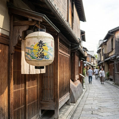 Traditional paper lantern japanese with spring ocean calligraphy and colorful wave designs hanging outside wooden storefront on historic Kyoto street during daytime