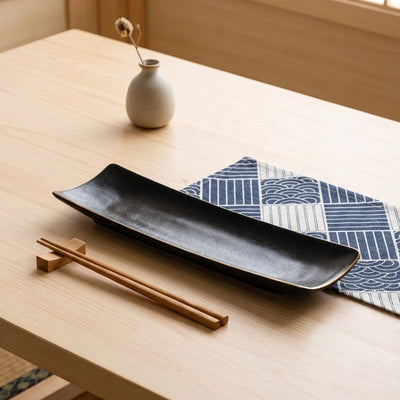 Handcrafted plate for sushi black with natural glaze finish on wooden surface with geometric table runner
