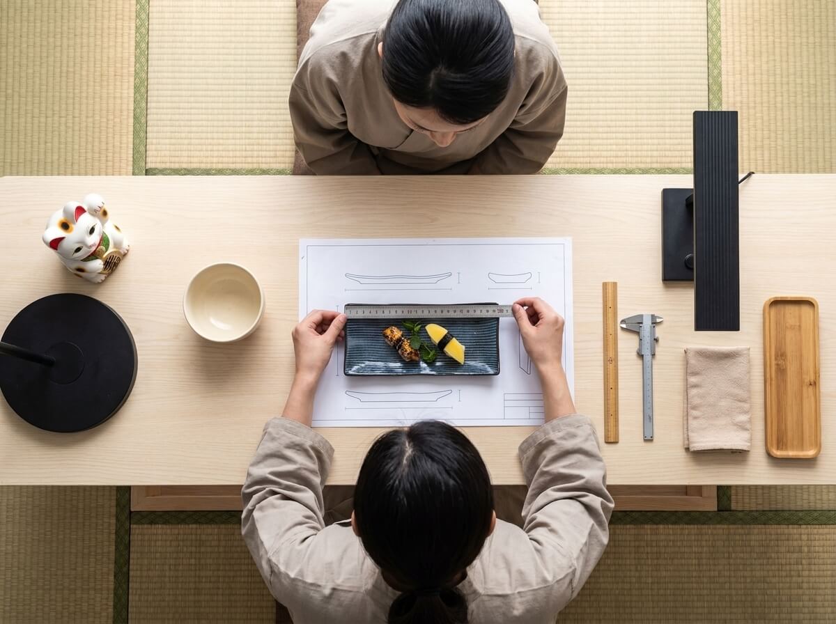 Overhead view of grilled eel and tamago nigiri arranged on a traditional plate of sushi, being measured against its blueprint in a tatami room