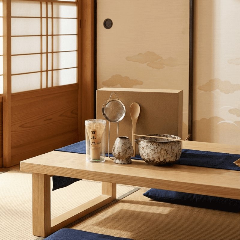Natural beige set for japanese matcha displayed on low table with navy blue cushion beside shoji screen and mountain landscape art