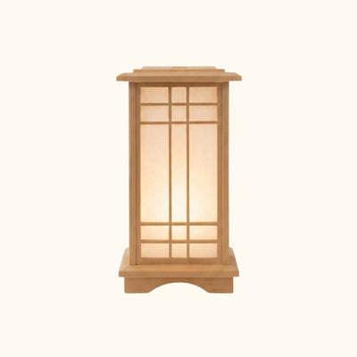 Front view of a small japanese style lamp with a wooden lattice frame and glowing paper panels, photographed on a clean studio background
