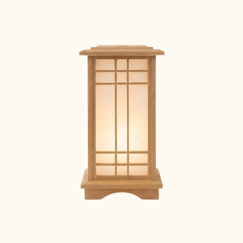Front view of a small japanese style lamp with a wooden lattice frame and glowing paper panels, photographed on a clean studio background