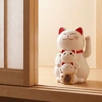 White solar maneki neko family of three on wooden windowsill near traditional shoji screen in bright natural daylight setting