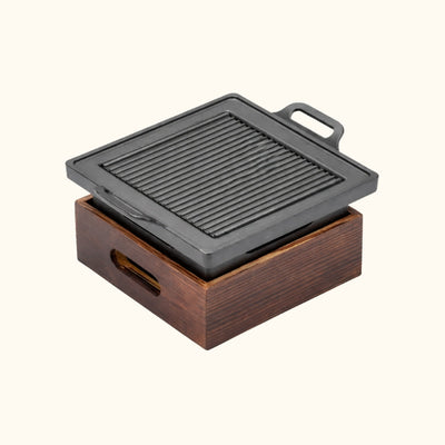 Square Japanese BBQ grill with compact cast iron cooking plate and ventilated wooden charcoal chamber on white background