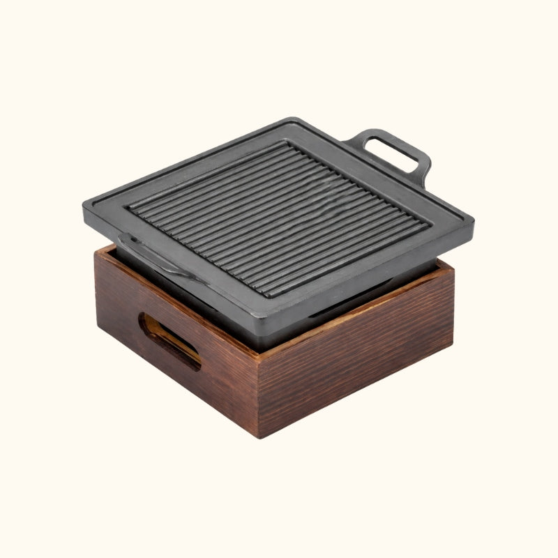 Square Japanese BBQ grill with compact cast iron cooking plate and ventilated wooden charcoal chamber on white background