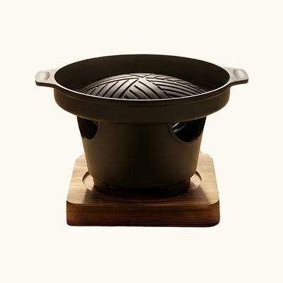 Style barbecue Japanese round ceramic grill with ridged cooking plate and side handles on wooden platform against neutral background