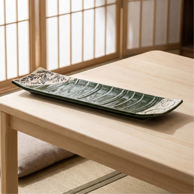 Long rectangular sushi plate with green glaze and botanical decorations on wooden chabudai table