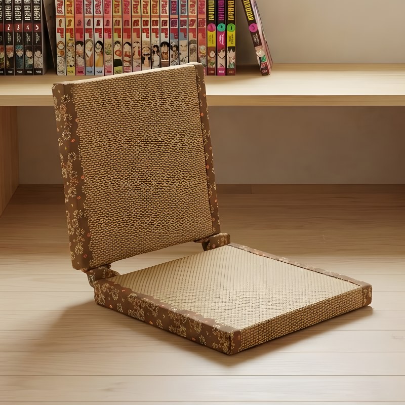 Tatami floor chair with brown reed weave and golden sakura embroidery border on light wood near bookshelf with manga