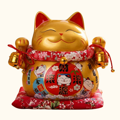 Front view of a lucky cat maneki neko gold statue with painted red ears, jingling bells, and fortune kanji on its belly, photographed on a clean studio background