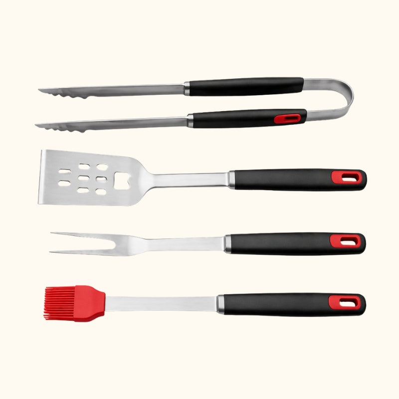 Four-piece tool set bbq featuring stainless steel tongs spatula fork and red silicone basting brush with black ergonomic handles on white background