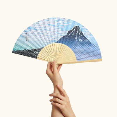 Beautiful traditional folding fan japanese with Mount Fuji pattern held delicately with both hands against minimalist white background highlighting landscape details