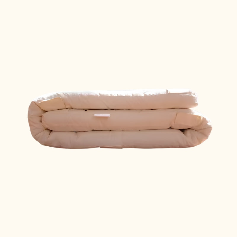 Thick traditional japanese futon neatly folded in soft beige quilted cotton on white background