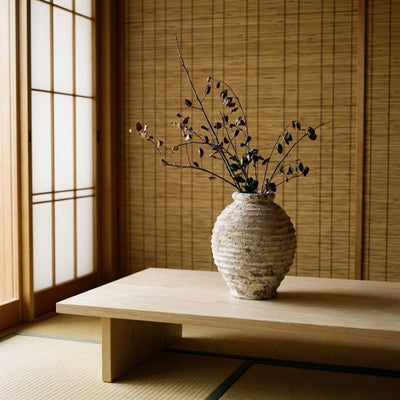 Rustic vase ceramic ikebana with horizontal ribbing holding dried botanicals on wooden table near bamboo blind