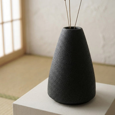 Minimalist vase ikebana flower arrangement with simple branches on fabric covered pedestal in zen interior