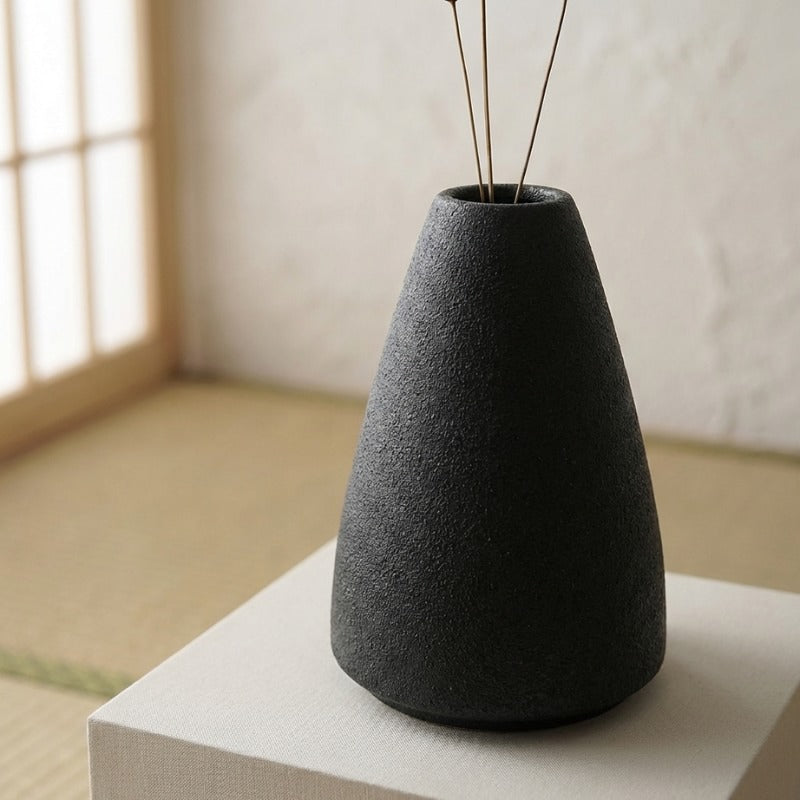 Minimalist vase ikebana flower arrangement with simple branches on fabric covered pedestal in zen interior