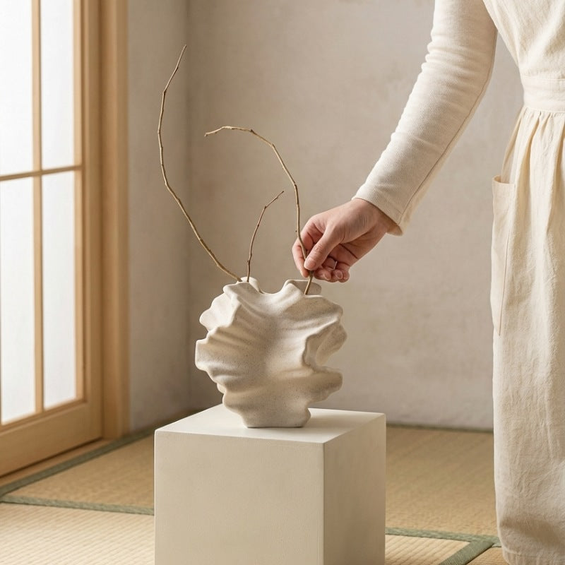 Hand arranging minimalist branches in sculptural vase japanese floral on white pedestal in zen interior