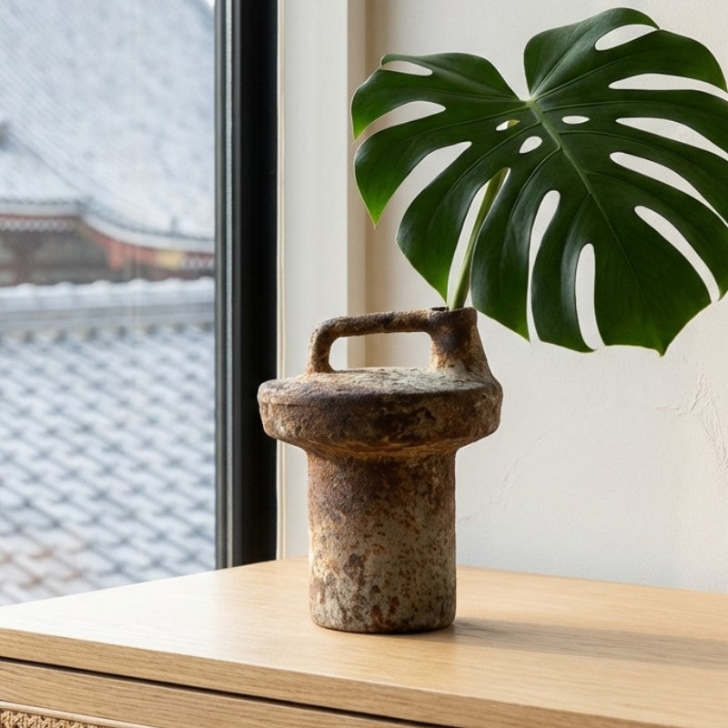 Textured vase wabi sabi with monstera leaf on modern shelf against window with temple architecture view