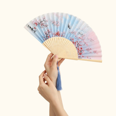 Elegant vintage hand fan japanese style with gradient cherry blossom design held gracefully showing natural bamboo frame and blue silk tassel