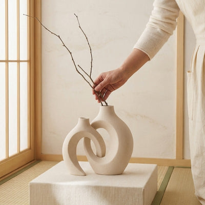Hand placing branches in artistic vintage white japanese vase displayed on fabric pedestal near tatami