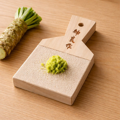 Traditional wasabi grinder in use with fresh wasabi root and grated green paste on natural wood surface