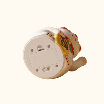 Underside of a white Japanese waving Maneki Neko cat showing its battery compartment and power switch.