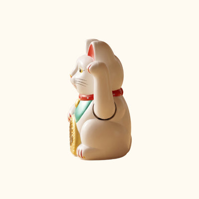 Side profile of a white waving Maneki Neko Japanese lucky cat with a raised paw, green bib and gold coin.