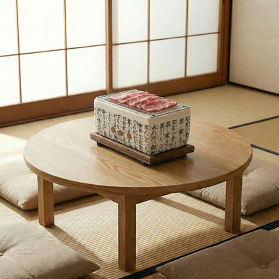 White barbecue Japanese ceramic grill with traditional script cooking thinly sliced wagyu on round wooden table with cushions