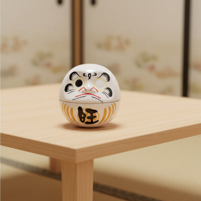 Small white daruma japan good luck charm with bold black eyebrows on modern wooden table near decorative screen