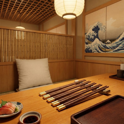 Five pairs of wood chopsticks in dark walnut with gold brass caps arranged on a low table in a traditional izakaya restaurant with bamboo panels, paper lantern, sashimi plate and a Great Wave mural