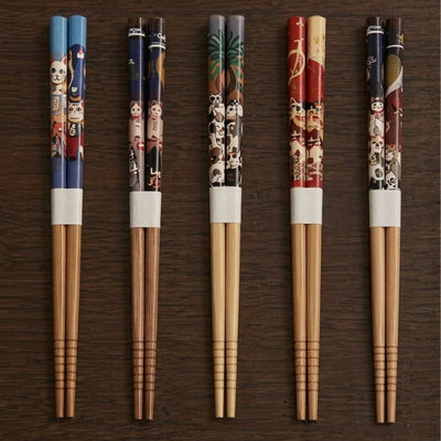 Five pairs of wood kawaii chopsticks with cat and character motifs stand upright against a dark wood background